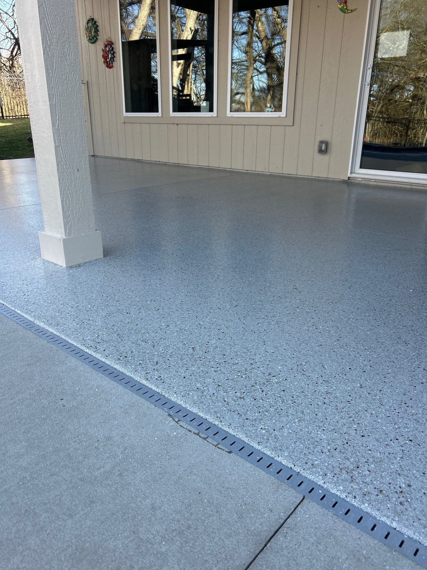 Outdoor Patio Concrete Epoxy Floor Coating Light gray speckled epoxy coating on an outdoor concrete patio with a drainage channel and house.