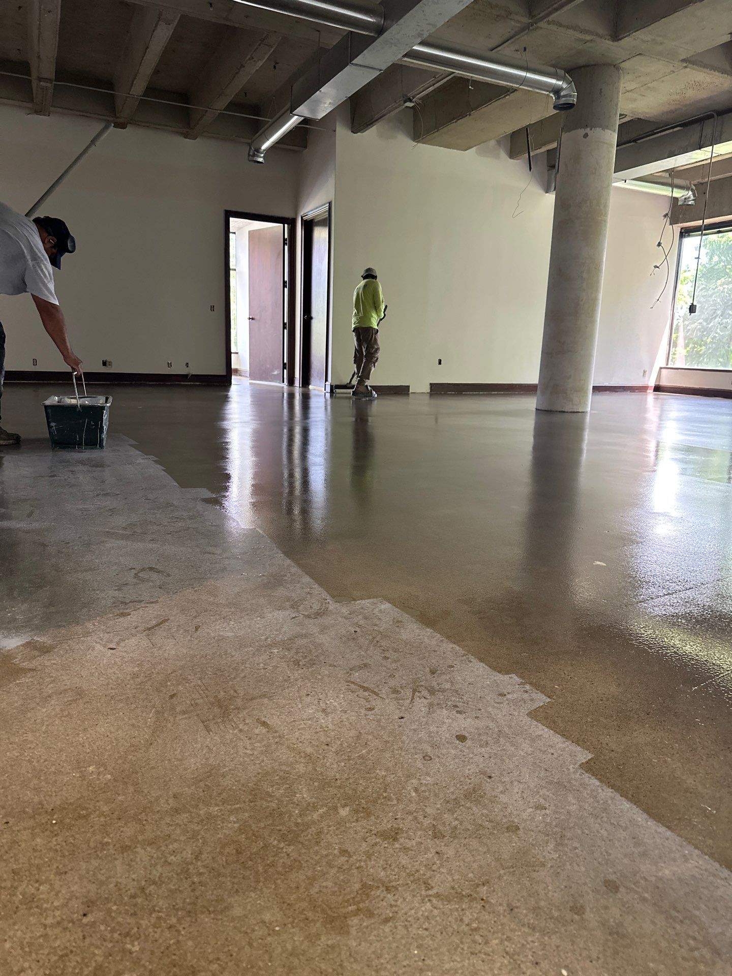 Commercial Epoxy Floor Application Wet tan epoxy coating applied to commercial floor with worker in yellow jacket and concrete support column