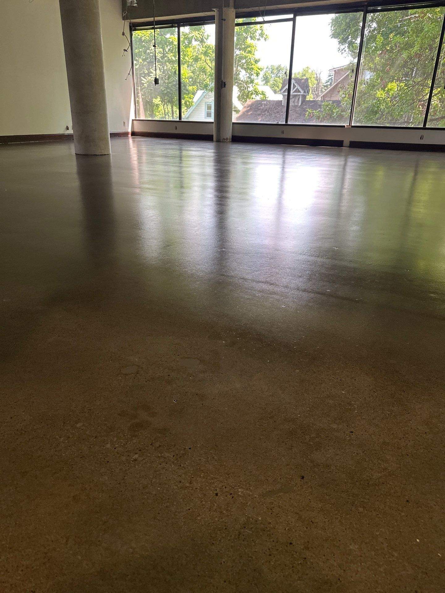 Commercial Epoxy Floor Installation Polished gray epoxy-coated concrete floor with glossy wet finish in commercial space with large windows and support column